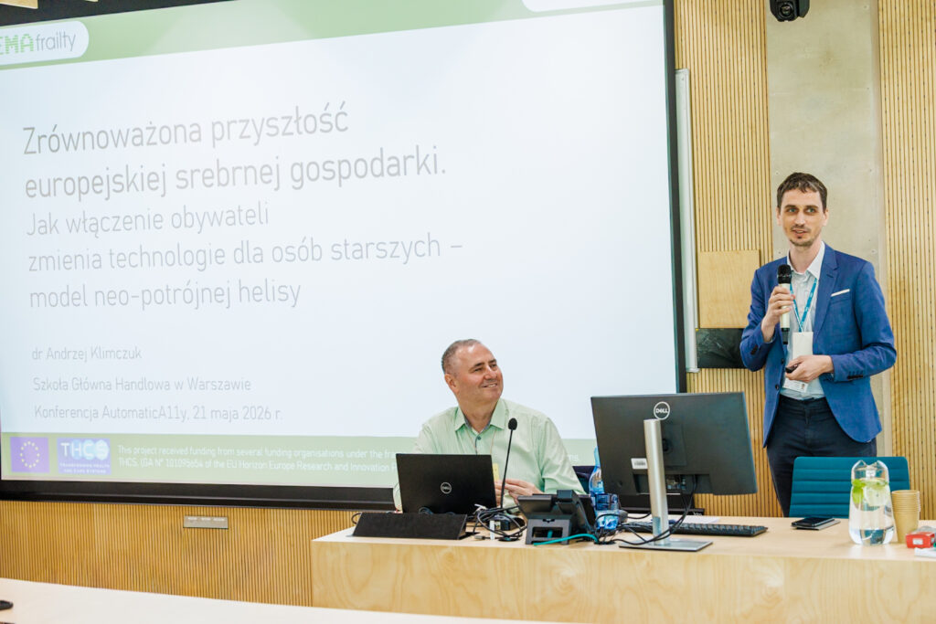 Dr Andrzej Klimczuk w niebieskiej marynarce przemawia do mikrofonu, w tle slajd tytułowy o europejskiej srebrnej gospodarce, przy stole siedzi Jacek Zadrożny.