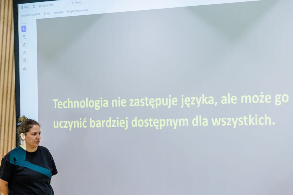 Ten sam slajd z cytatem o technologii i języku, na pierwszym planie kobieta w czarnej bluzce z aparatem słuchowym.