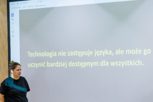 Ten sam slajd z cytatem o technologii i języku, na pierwszym planie kobieta w czarnej bluzce z aparatem słuchowym.