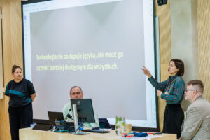 Slajd z cytatem o technologii i dostępności języka, Natalia Pacyga tłumaczy na język migowy, obok kobieta w czarnym stroju i mężczyzna w kraciastej marynarce.